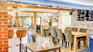 Un interior de restaurante con mesas y sillas de madera, un muro de ladrillo y una lámpara de araña.