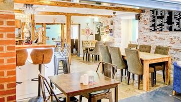 A restaurant interior with wooden tables and chairs, a brick wall, and a chandelier.