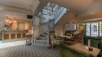 A hotel lobby with a staircase, seating area, and a reception desk.