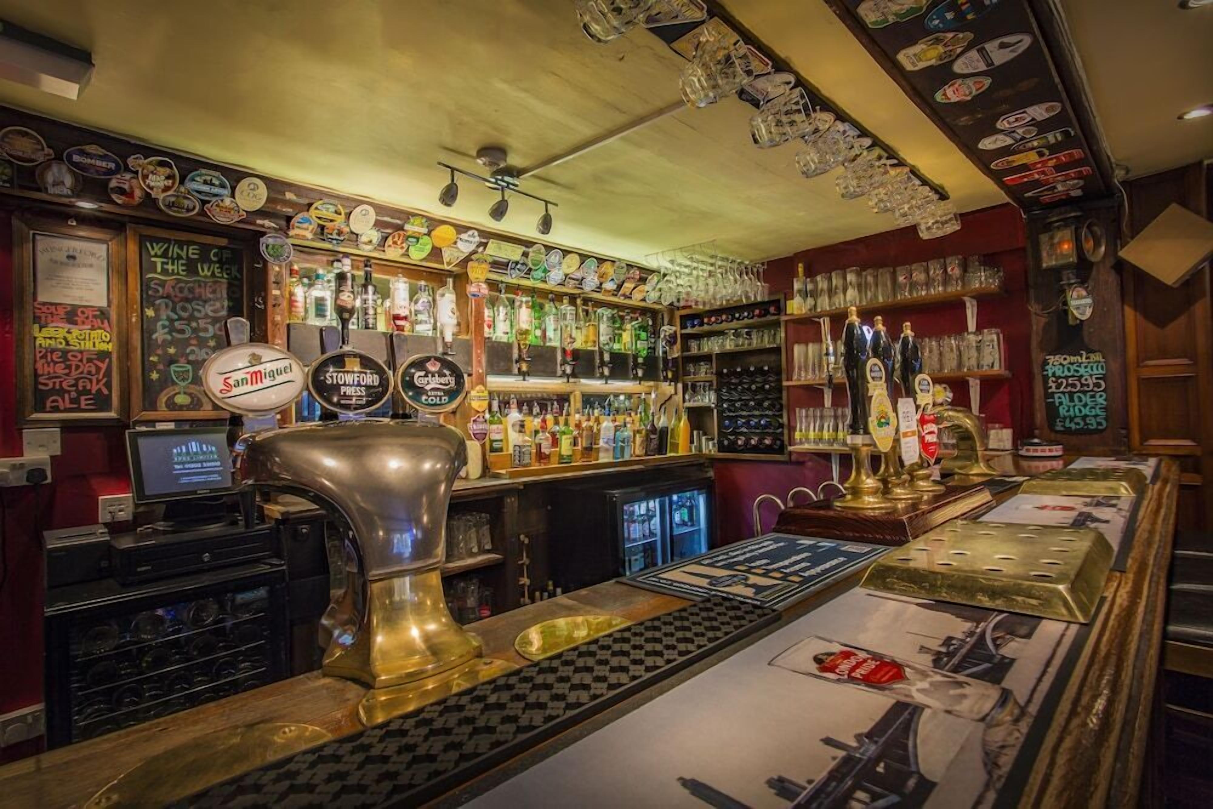En bar med et udvalg af flasker og glas på hylder, et fadølsanlæg og en jukebox.