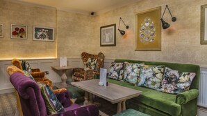 Une pièce chaleureuse avec un canapé vert, un fauteuil violet et une table en bois. Des tableaux encadrés ornent les murs et une lampe est suspendue au-dessus du canapé.