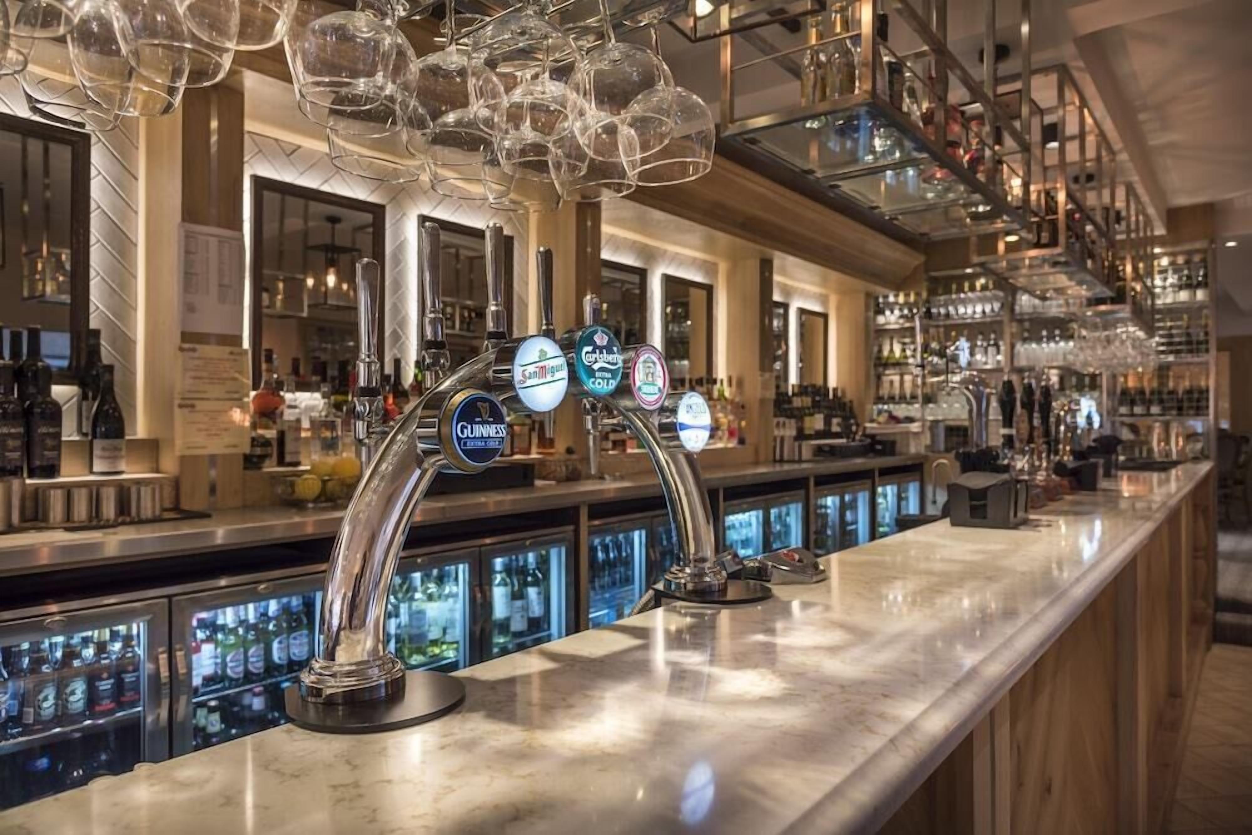 A bar area with multiple taps, including brands like Guinness and San Miguel, and a well-stocked shelf with various bottles.