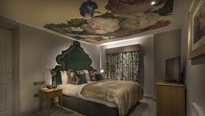 Une chambre à coucher avec un grand lit, une table de chevet, un téléviseur et une fresque murale au plafond.