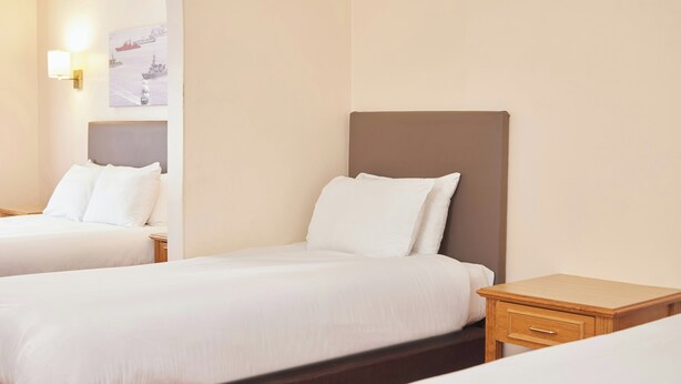 A hotel room with two beds, a nightstand, a lamp, and a wall-mounted artwork. - The Farmhouse Innlodge (Portsmouth)