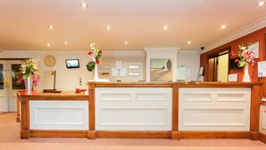 A reception desk with a clock, a television, and a bulletin board. - The Farmhouse Innlodge (Portsmouth)