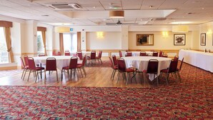 A conference room with round tables and red chairs, carpeted floor, and a large window with curtains. - The Farmhouse Innlodge (Portsmouth)