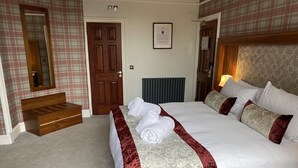 A hotel room with a large bed, a wooden bench, a mirror, a door, and a framed notice on the wall. - Craigiebield House Hotel (Penicuik)