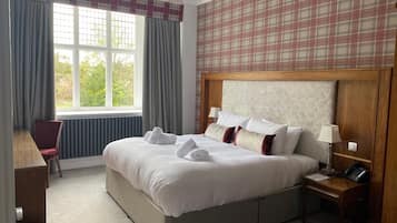 A hotel room with a large bed, a desk, a chair, a bedside table, and a window with curtains.
