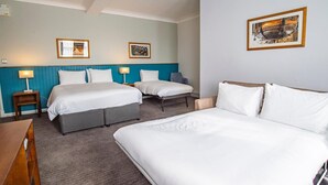 Ett hotellrum med två sängar, ett skrivbord och en stol. Det finns inramade tavlor på väggen och en lampa på skrivbordet.