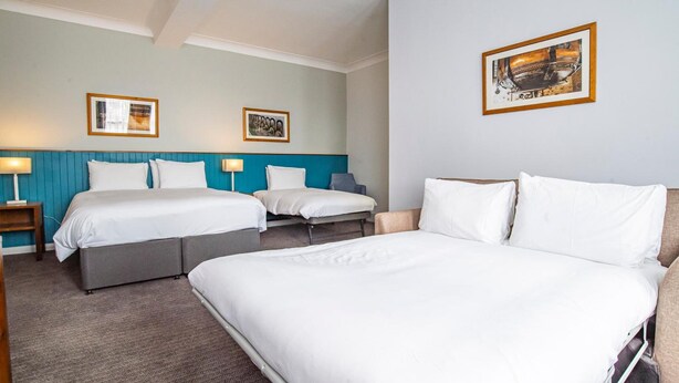 Ett hotellrum med två sängar, en stor säng i förgrunden och en mindre i bakgrunden. Det finns två sängbord med lampor, ett konstverk som hänger på väggen och ett rum med heltäckningsmatta.