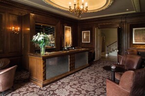A reception area with a wooden reception desk, a chandelier, and a patterned carpet. - Wood Hall Hotel & Spa (Wetherby)