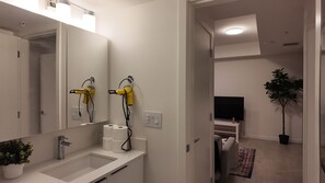 Casa de banho moderna com lavatório, espelho e dois secadores de cabelo fixados na parede.