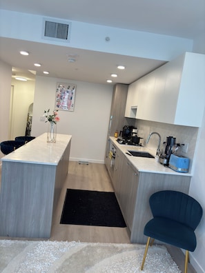 A modern kitchen with a central island, built-in appliances, and a dark blue chair. - Cozy 2-bedroom apartment with AC in peaceful Surrey (Surrey)