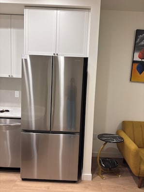 A stainless steel refrigerator with a freezer compartment, a kitchen counter, and a small round table with a black marble top. - Cozy 2-bedroom apartment with AC in peaceful Surrey (Surrey)
