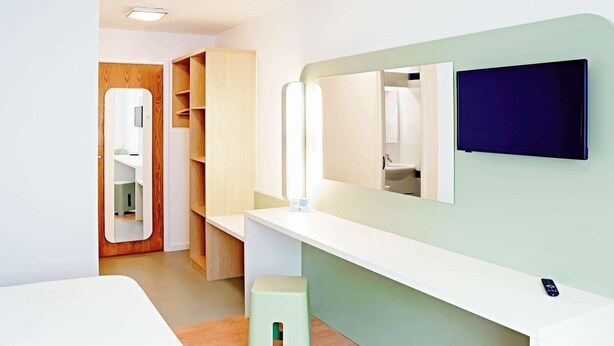 Un dormitorio moderno con una cama, un tocador con espejo, un taburete pequeño y un armario.