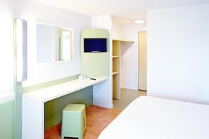 Una habitación de hotel moderna con una cama blanca, un taburete pequeño, un espejo, un televisor y una puerta de madera.