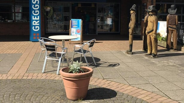 Un edificio con un letrero que dice 'Greggs' y mesas con sillas al aire libre.
