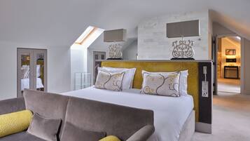 A modern bedroom with a large bed, a sofa, a glass shelving unit, and a view of a bathroom.