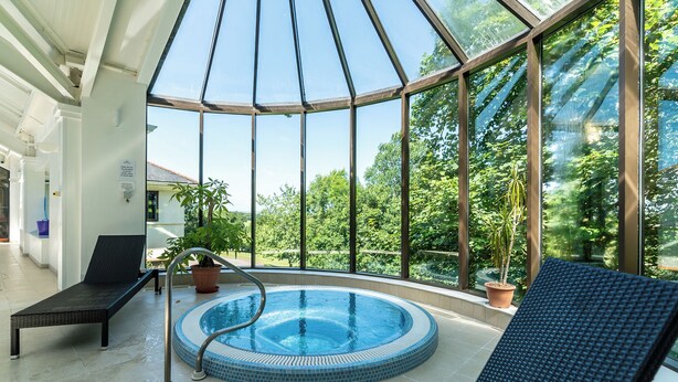 A glass-enclosed indoor pool area with lounge chairs, a hot tub, and potted plants. - The Mole Resort (Umberleigh)