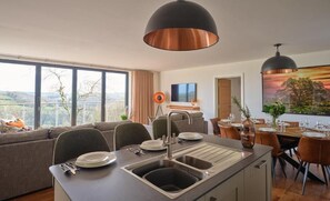 Uma cozinha moderna com ilha central, área de jantar com vista e uma janela grande para um horizonte.