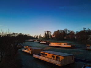 A series of wooden cabins with attached balconies, set in a hilly area with trees in the background. - The Mole Resort (Umberleigh)