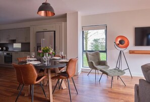 A modern kitchen with a dining area, a large window, and a floor lamp. - The Mole Resort (Umberleigh)