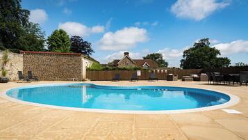 A swimming pool with lounge chairs, a stone wall, and a house in the background.