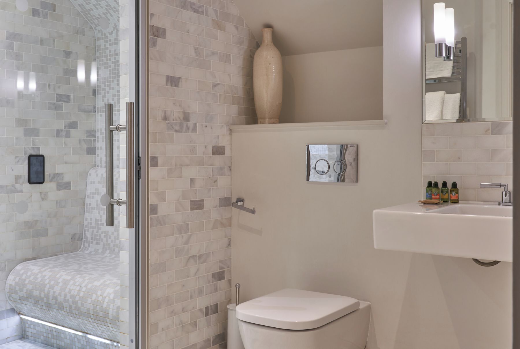 A bathroom with a glass shower enclosure, a toilet, a sink with toiletries, and a mirror.