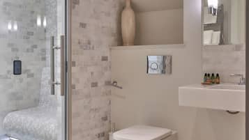 A bathroom with a glass shower enclosure, a toilet, a sink with toiletries, and a mirror.