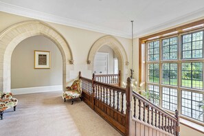 A grand staircase with a wooden railing, a carpeted floor, and a view of a lush garden through large windows. - The Mole Resort (Umberleigh)