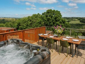 A wooden deck with a hot tub, dining table, chairs, and a view of the countryside. - The Mole Resort (Umberleigh)