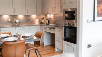 Una cocina moderna con armarios blancos, una zona de comedor con una mesa y sillas de madera, y un horno empotrado.