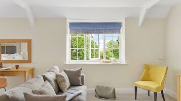 A room with a large window, a sofa, a yellow chair, a small table, and a mirror.