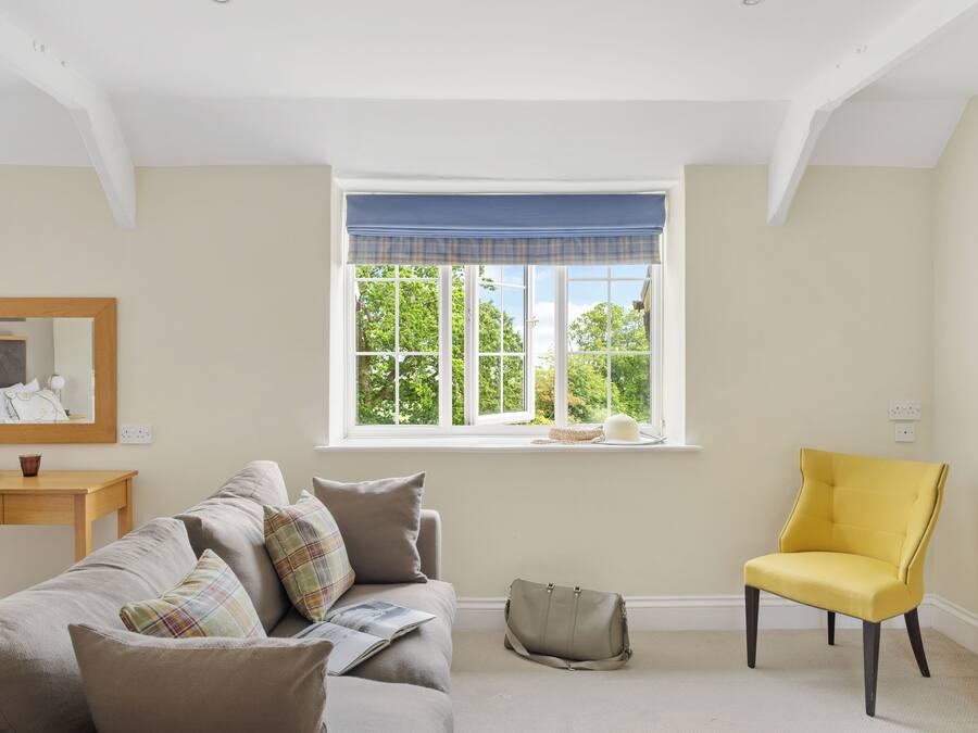 Una habitación con un ventanal grande, un sofá, un sillón amarillo, una mesita y un espejo.