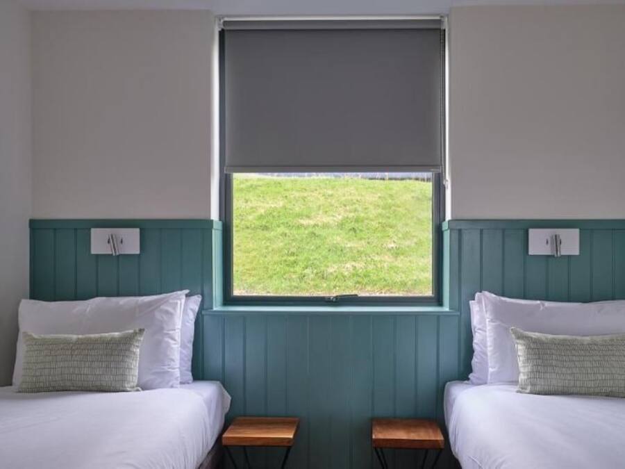 A room with two beds, a window, and a view of a grassy area.