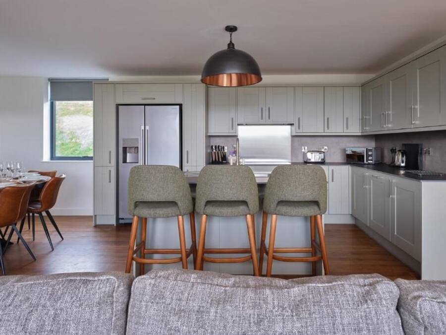 A modern kitchen with grey cabinets, a central island with stools, and a dining area with a table set for four.