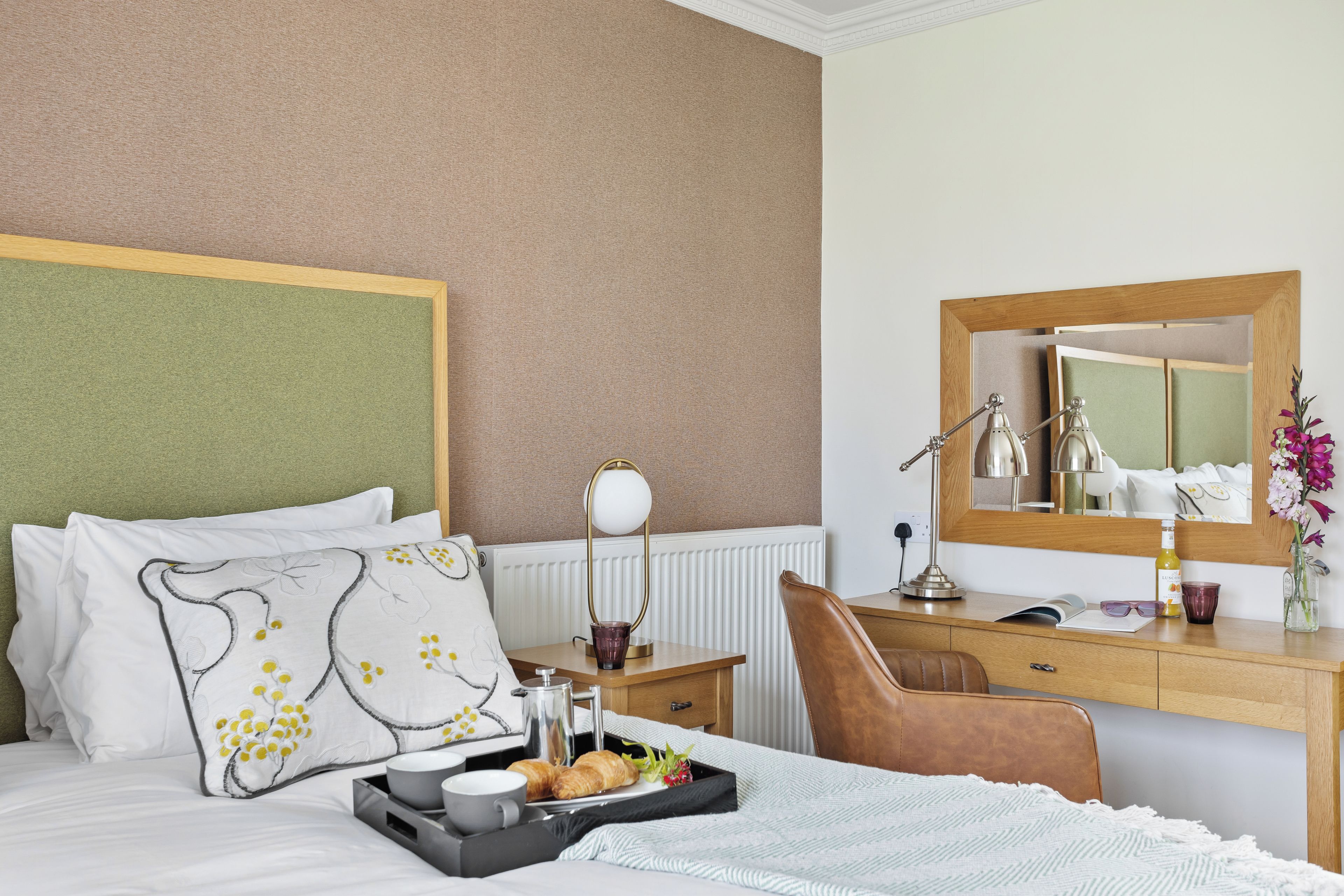 A hotel room with a bed, a desk, a chair, a mirror, and a tray with breakfast items.