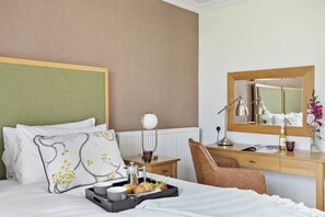 A hotel room with a bed, a desk, a chair, a mirror, and a tray with breakfast items.