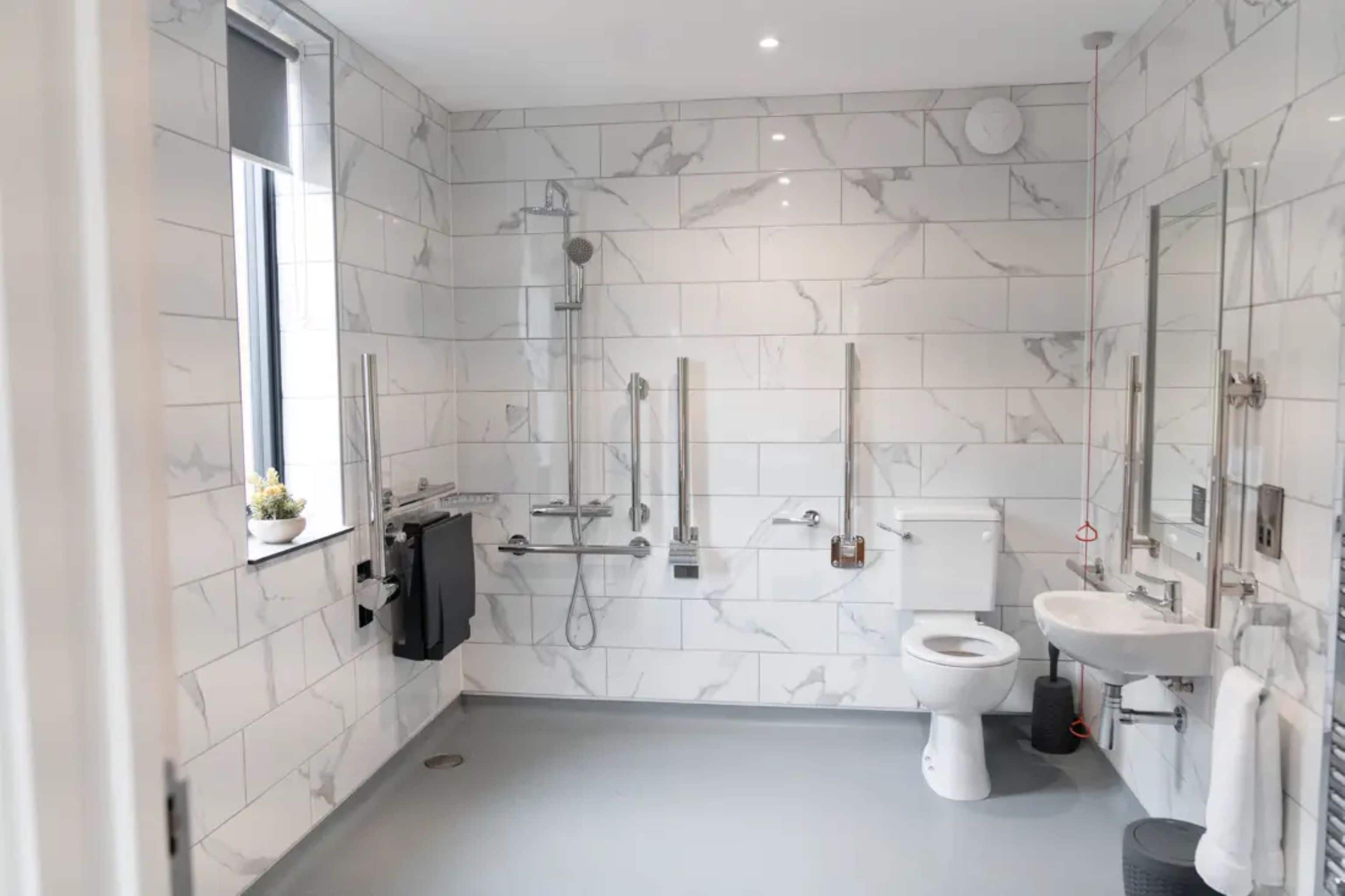 A modern bathroom with a toilet, bidet, and sink, marble tiles, and a window.