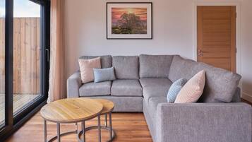 A grey sofa with multiple cushions, a round wooden coffee table, and a framed picture on the wall.