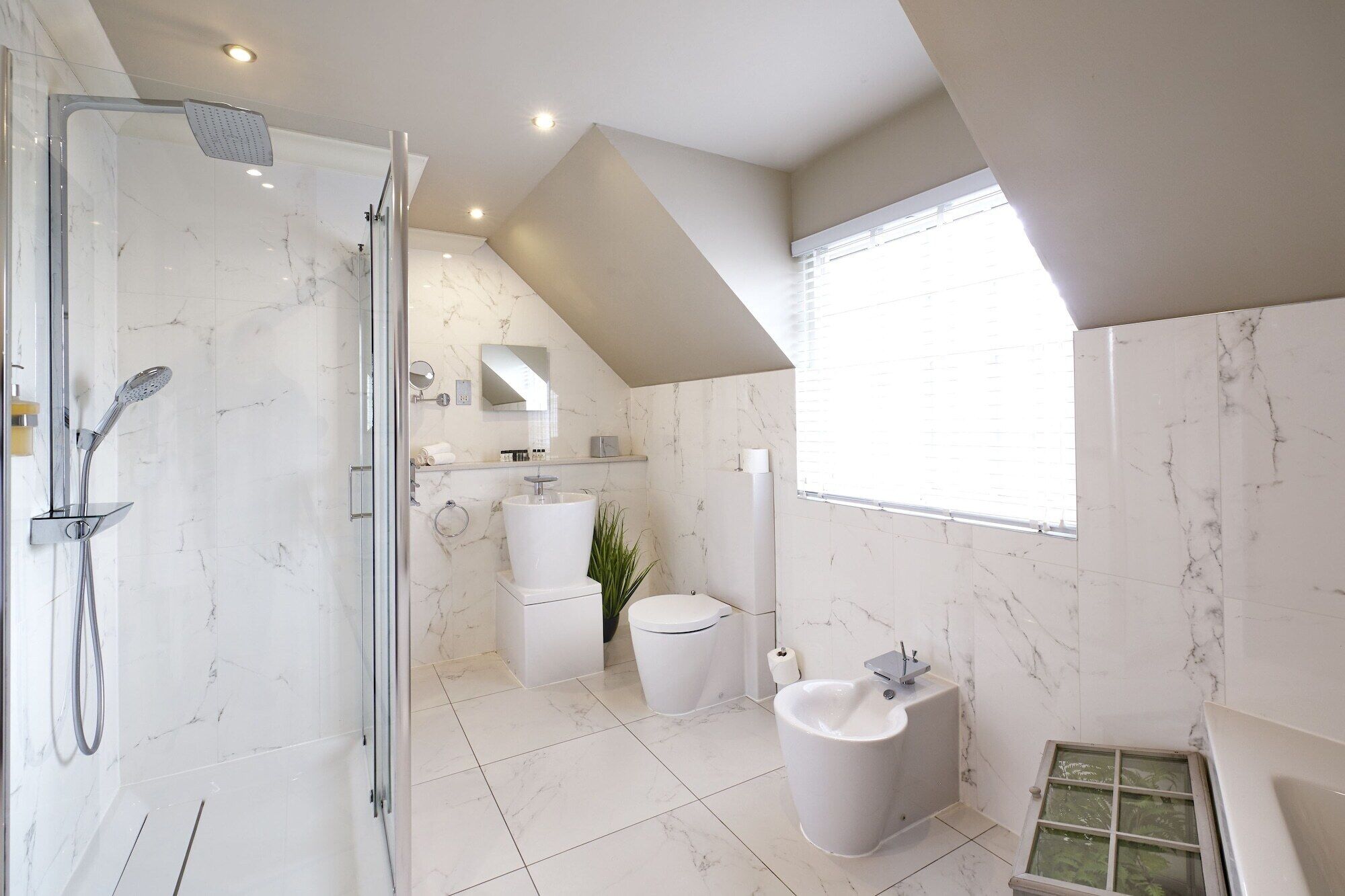 A modern bathroom with a glass-enclosed shower, a pedestal sink, and a bidet.