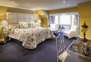 Una habitación de hotel con una cama grande, dos sillas, una mesita y una lámpara.