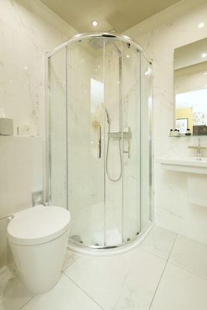 Un baño moderno con ducha envuelta en vidrio, inodoro blanco y tocador con espejo.