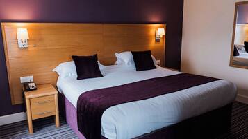 A hotel room with a bed, bedside table, lamp, and a mirror on the wall.