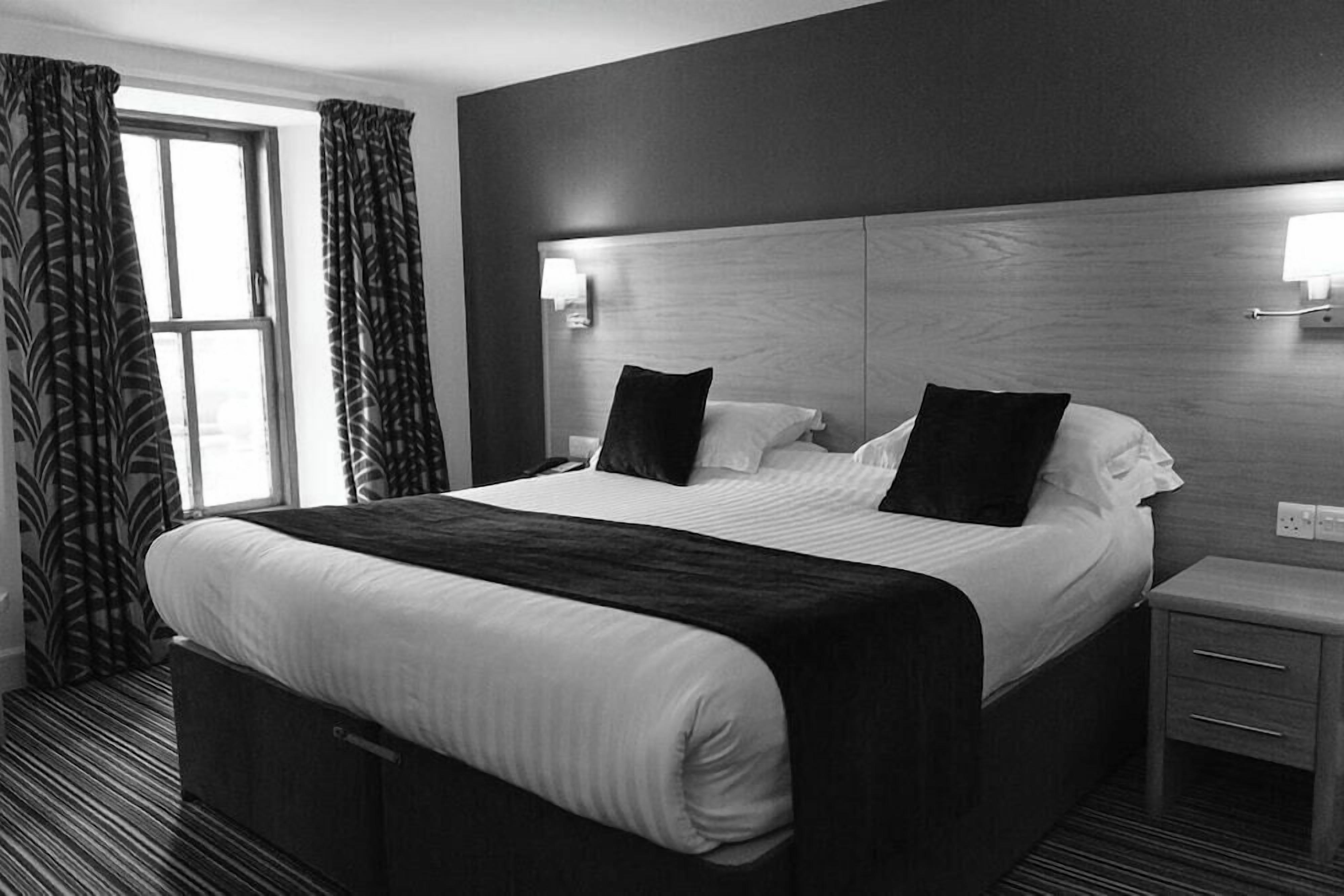 A hotel room with a large bed, two bedside tables, a nightstand, and a window with curtains.