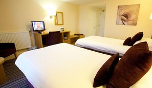 Ein Hotelzimmer mit zwei Betten, einem Schreibtisch, einem Sessel, einem Fernseher und einem Bild an der Wand.
