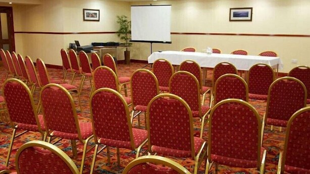 Ein Konferenzraum mit Reihen roter Stühle, einer Tafel und einer Projektionsleinwand.