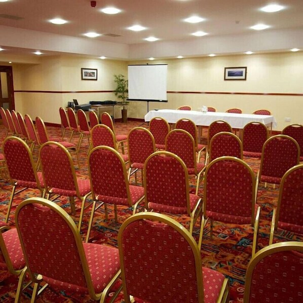 A conference room with rows of red chairs, a whiteboard, and a projector screen. - Ayre Hotel (Kirkwall)