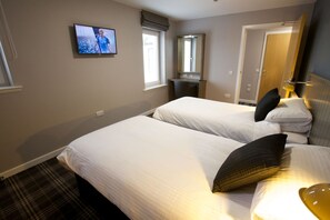 Ein Hotelzimmer mit zwei Betten, einem an der Wand befestigten Fernseher, einem Spiegel und einer Tür.