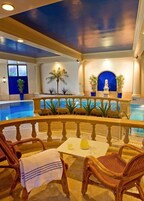 Un área junto a la piscina con sillas de mimbre, una mesa con jarras de agua y vista al estanque.